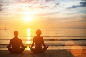 2 pessoas meditando na praia